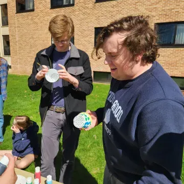 two students outside painting pots